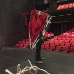 Cultch Residency 2022. York Theatre. black pants and brown shoes prop up a wire tooth costume against the backdrop or red theatre seats. a red yarn heart drapes down the side. a bare wire tooth structure lays on the black floor in the foreground